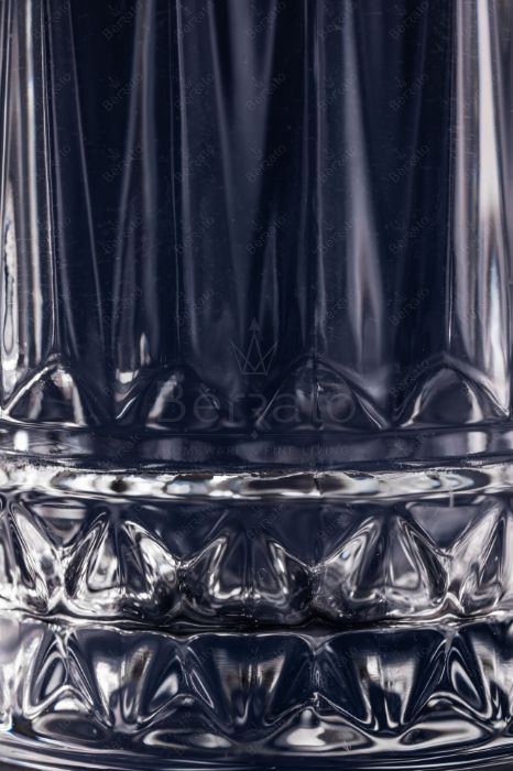 نمای نزدیک از لیوان بلند الیزه مدل SMW6022 با تراش‌های عمودی نیزه‌ای و پایه چهارخانه درخشان بر روی پس‌زمینه تیره.